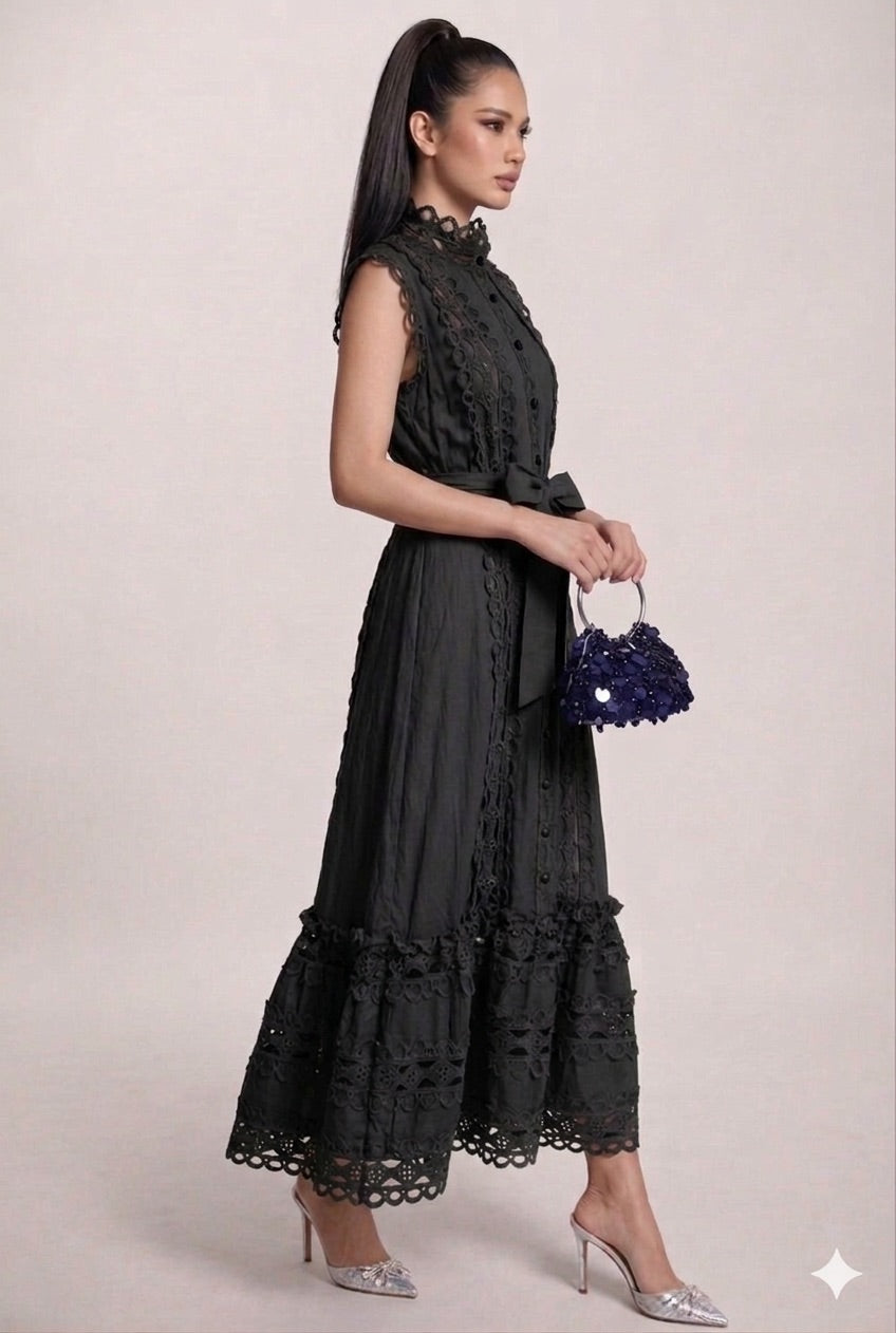 Woman wearing a black lace dress holding a matching handbag against a light background