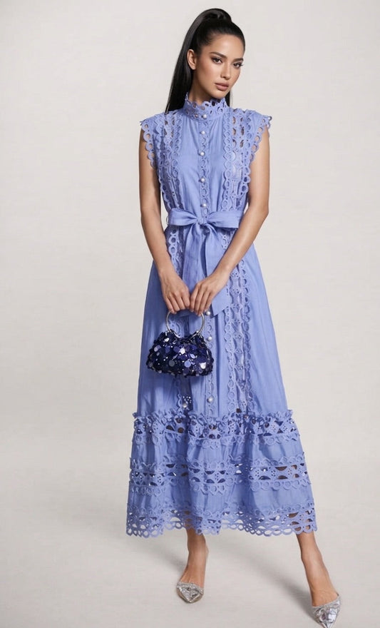 Woman wearing a blue dress holding a matching handbag on a plain background