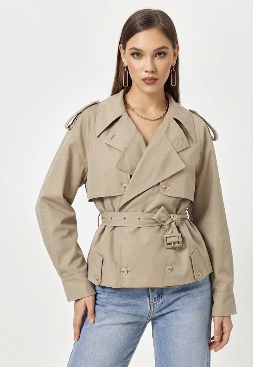 Woman wearing a beige trench coat and blue jeans on a white background